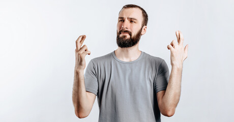 Naklejka premium Handsome young man frown and cross fingers in hope on white background with space for advertising mock up