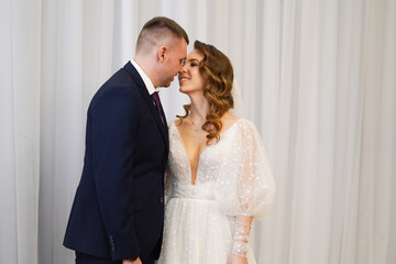 Fototapeta premium beautiful and happy bride and groom against the background of the white curtain