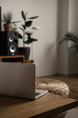 Aesthetic minimal home, living room interior design. Wooden table with laptop computer, rattan pouf, stereo system. Home office desk workspace. Blog, web, social media concept. Work at home.