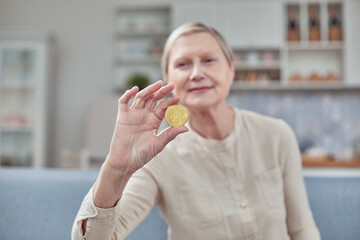 An elderly woman holds a bitcoin coin in her hand. Happy retirement life concept