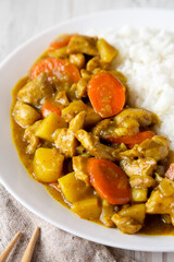 Homemade Japanese Chicken Curry  on a white plate on a white wooden background, low angle view. Close-up.