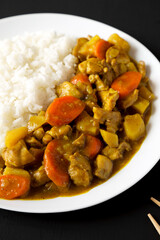 Homemade Japanese Chicken Curry  on a white plate on a black background, side view.