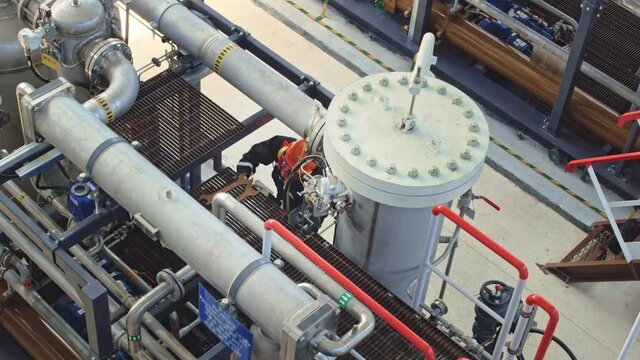 A mechanic removes large wrenches after repairing equipment. The employee is dressed in a black uniform, an orange hard hat, safety glasses and earmuffs. Work at an oil refinery.