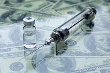 Glass syringe and vial with vaccine against the background of american dollars