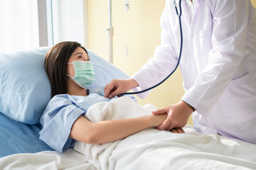 Fototapeta premium Women Asian doctors hold the patient hand and encourage and provide medical advice While doctors use Stethoscope for checking the patient heart in bed. Concept of Care and compassion