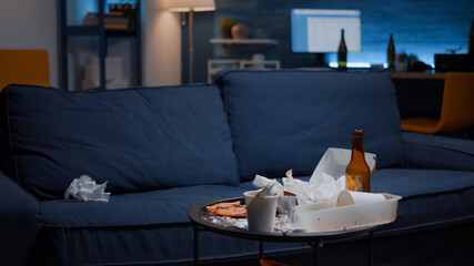 Close up of messy table with leftover in empty unorganized living room of depresive person. House apartment of alone woman with sever depresion having trash, rubbish, napkins on blue sofa