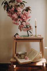 a small wooden staircase with a transparent vase and blooming pink branches. composition of sakura branches in a transparent vase and an open book with a cup of coffee. pink sakura petals. copy space