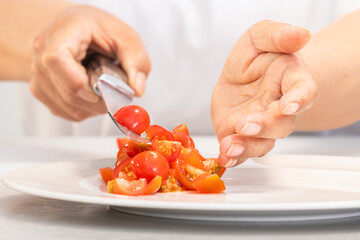 Obraz na płótnie Canvas Hands dropping freshly cut tomatoes on a plate