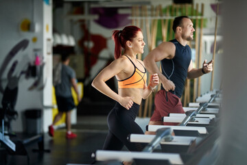 Athletic couple running on treadmills while working out in a gym.