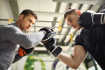 Below view of young fighter exercising with a coach during sports training at the gym.