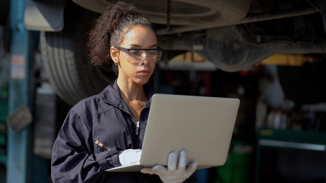 african american mechanic woman using laptop computer  checking list to undercarriage of car in workshop at auto car repair service center with lift . car engineer female inspection vehicle details
