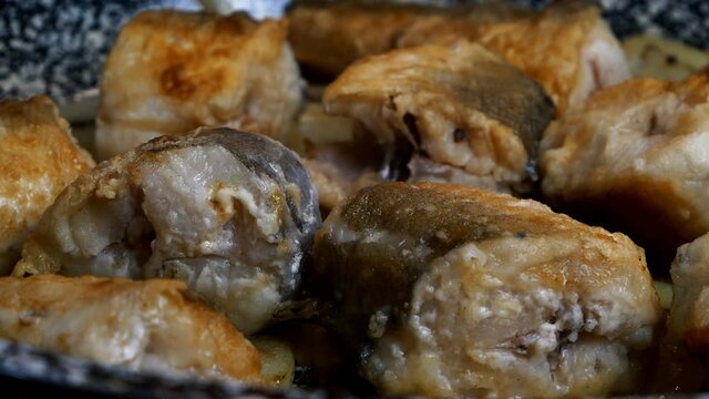 Cooking white sea fish hake, cut into pieces in frying pan. Baked hake or pollock with golden crust.