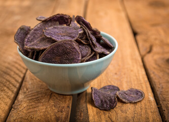 Potato chips made from purple potatoes in a bowl on rustic wooden table
