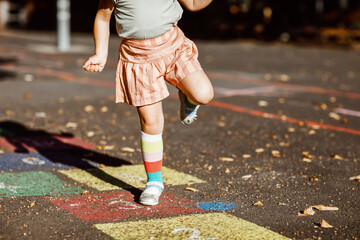 Closeup of leggs of little toddler girl playing hopscotch game drawn with colorful chalks on asphalt. Little active child jumping on playground outdoors on a sunny day. Summer activities for children.