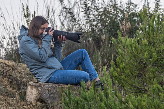 Young girl photographer with a camera and a large telephoto lens photographing wildlife