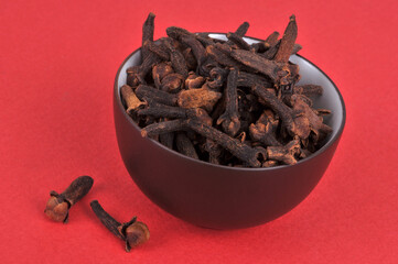 Bol de clous de girofle en gros plan sur fond rouge