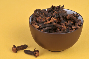 Bol de clous de girofle en gros plan sur fond jaune