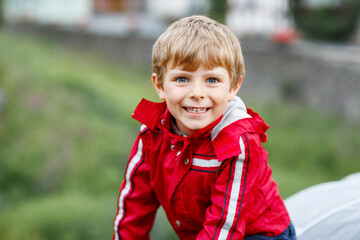 Little blond kid boy walking outdoors on rainy day. Portrait of cute preschool child having fun wear colorful waterproof clothes. Outdoor leisure walk on bad weather day with kids.