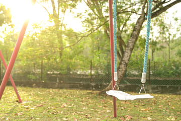 Empty playground with swing. Public park with trees and morning sun at the background. 