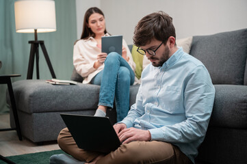 Home office of a young couple of employees, the girl works using a tablet, the guy a laptop