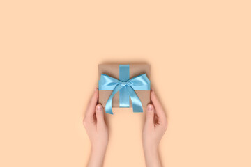 Female hands hold gift box on a beige background. Present tied with a blue ribbon. Romantic concept with copyspace.
