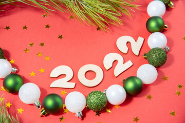 Wooden numbers 2022, pine branches and toy balls on a red paper background. Beautiful new year or christmas card top view