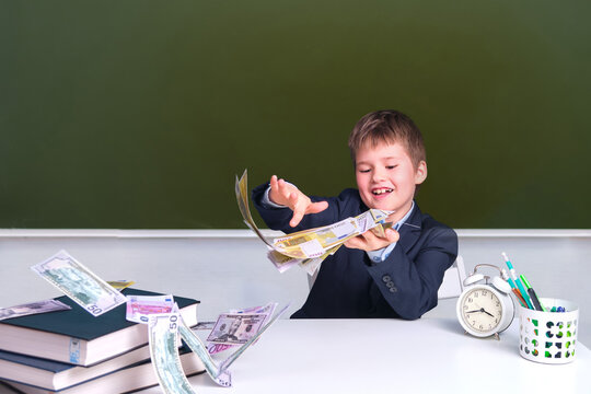 Junior Boy In A School Uniform At A Desk With Money In Dollars And Euros