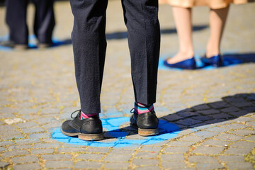 Shallow depth of field (selective focus) details with feet of people standing on special spots for social distancing at an event, during the Covid-19 outbreak.