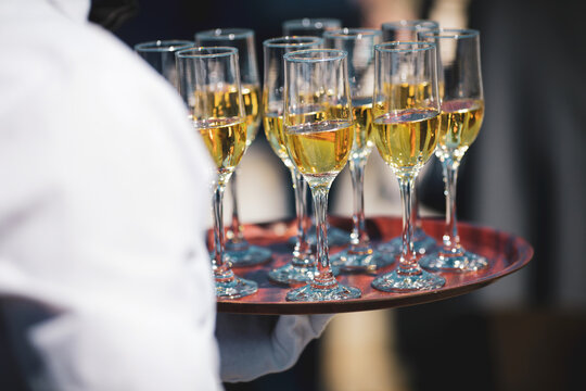 Shallow depth of field (selective focus) details with a waiter walking around and giving sparkling wine to the guests of an event.