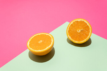 Two slices of fresh orange standing on the turquoise edge against warm pink background. Minimal sunlit flat lay summer fruit concept.