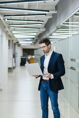 Fototapeta premium Young business man in office work online on laptop solve business problem. Pensive businessman use computer thinking pondering over project. 