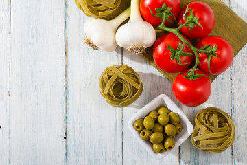 fresh tomato, garlic, olive, uncooked tagliatelle pasta on white wooden table, top view