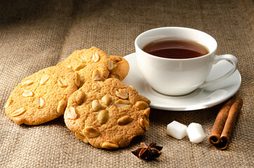 Cookies with peanuts on burlap. with a cup of tea, sugar cubes and a cinnamon stick. Appetizing sweets for tea at home