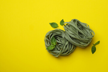 Uncooked green pasta and basil on yellow background