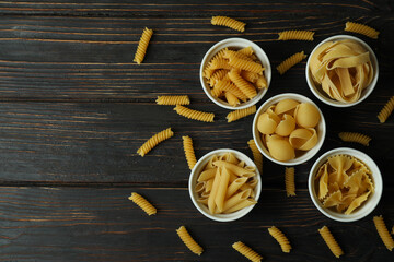 Bowls with uncooked pasta on wooden background