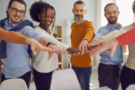 Happy diverse business team members put hands together after corporate meeting. Group of smiling multiracial business people, teammates and friends join hands as symbol of teamwork and participation