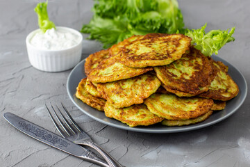 Fritters from zucchini in grey plate with sour cream sauce and greens. Vegetable pancakes of courgettes with green salad