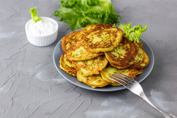 Fritters from zucchini in grey plate with sour cream sauce and greens. Vegetable pancakes of courgettes with green salad