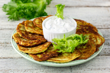 Fritters from zucchini with sour cream sauce and greens. Vegetable pancakes of courgettes with green salad