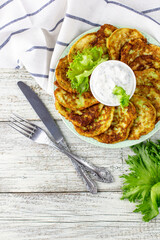 Fritters from zucchini with sour cream sauce and greens. Vegetable pancakes of courgettes with green salad