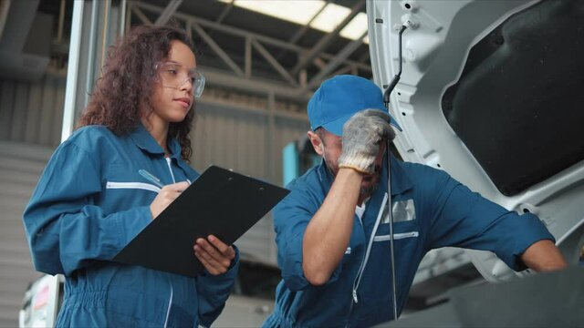 Two Auto mechanic checking car engine and taking notes in car auto repair service center. Car repair and maintenance. Car mechanic working at automotive service center.