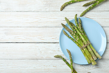 Plate with green asparagus on wooden background
