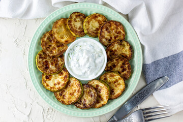 Fried slices of zucchini with sour cream sauce on plate. Fried courgettes with herb for dinner on white background