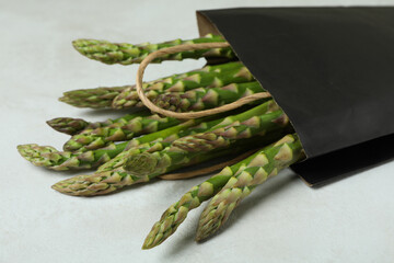 Bag with green asparagus on white textured background