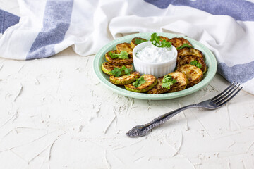Fried slices of zucchini with sour cream sauce on plate. Fried courgettes with herb for dinner on white background