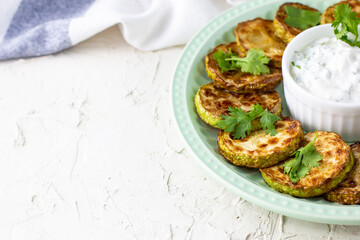Fried slices of zucchini with sour cream sauce on plate. Fried courgettes with herb for dinner on white background