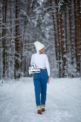 Fototapeta na wymiar Young blond beautiful female with white ice skates in her hand in winter snowy forest.