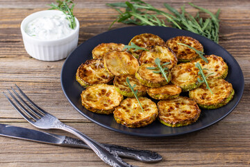 Fried slices of zucchini with sour cream sauce. Courgettes with herb for dinner on natural wooden background