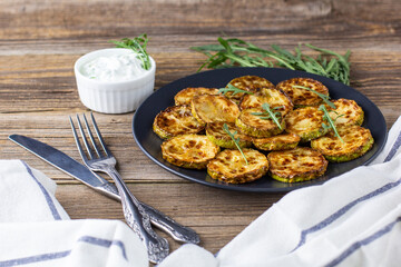 Fried slices of zucchini with sour cream sauce. Courgettes with herb for dinner on natural wooden background