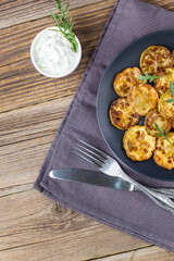 Fried slices of zucchini with sour cream sauce. Courgettes with herb for dinner on natural wooden background